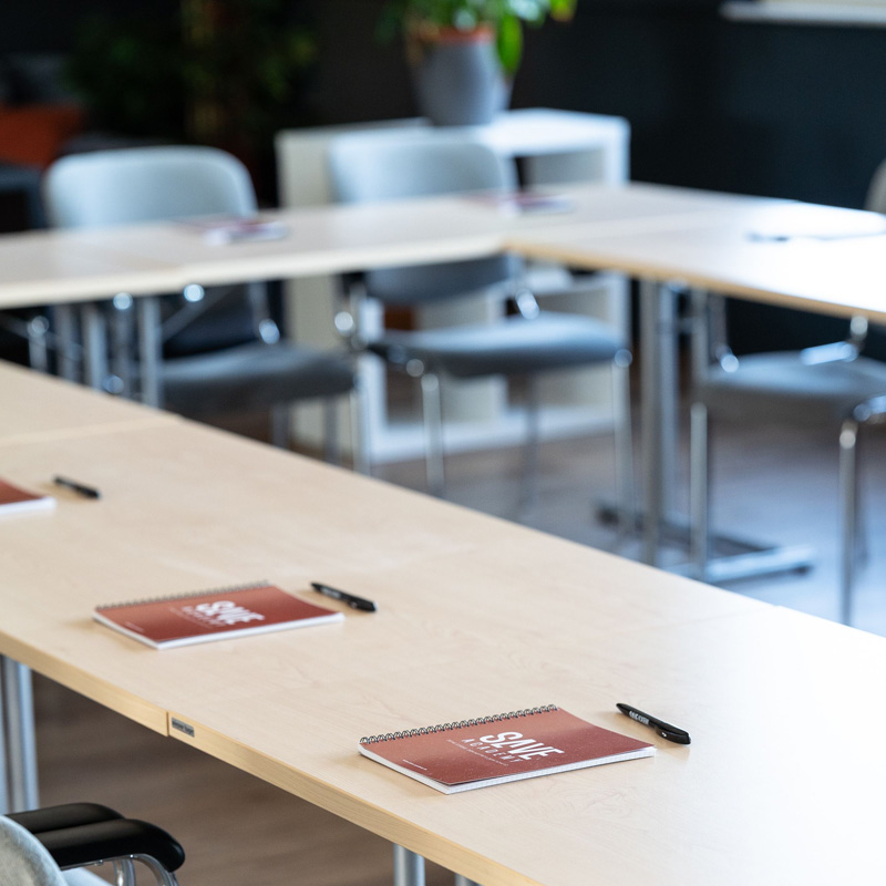Seminartische im SAVE Trainingszentrum, auf den Tischen liegen Blöcke und Stifte mit SAVE-Logo