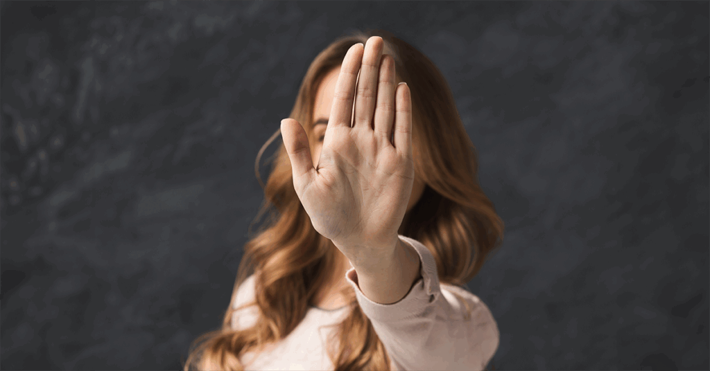 Frau vor dunklem Hintergrund, die die Hand ausgestreckt vor ihr Gesicht hält